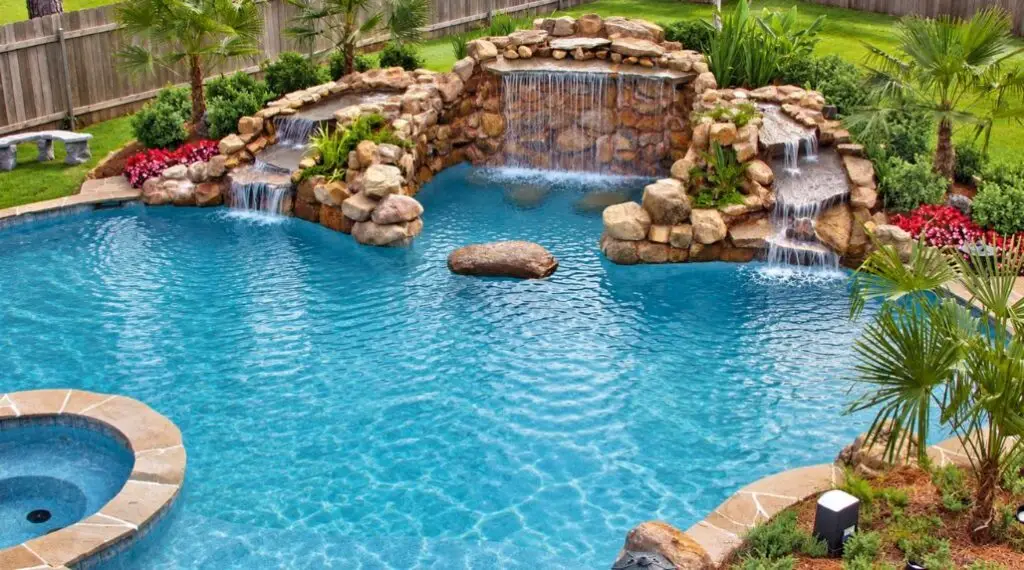 Freeform backyard swimming pool featuring natural rock waterfalls, a built-in spa, and tropical landscaping.