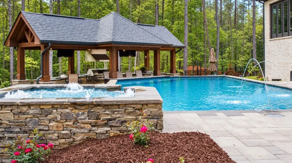 Backyard swimming pool and raised spa with stonework, outdoor kitchen pavilion, and coordinated landscaping