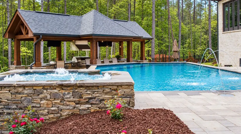 Backyard swimming pool and raised spa with stonework, outdoor kitchen pavilion, and coordinated landscaping