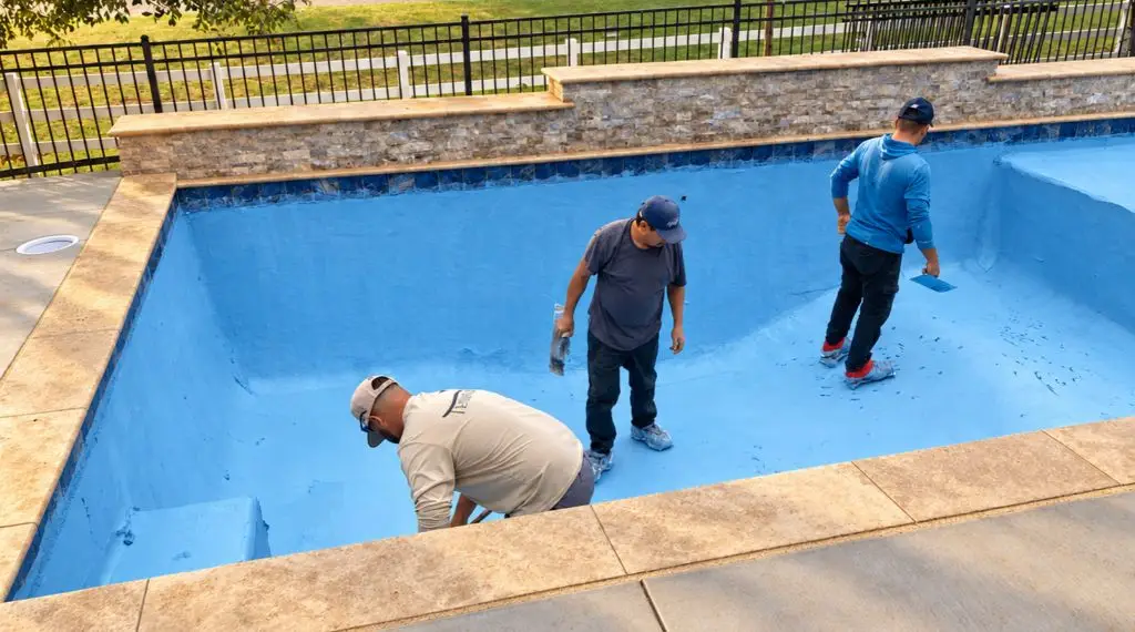 Workers applying a blue interior finish to a gunite swimming pool