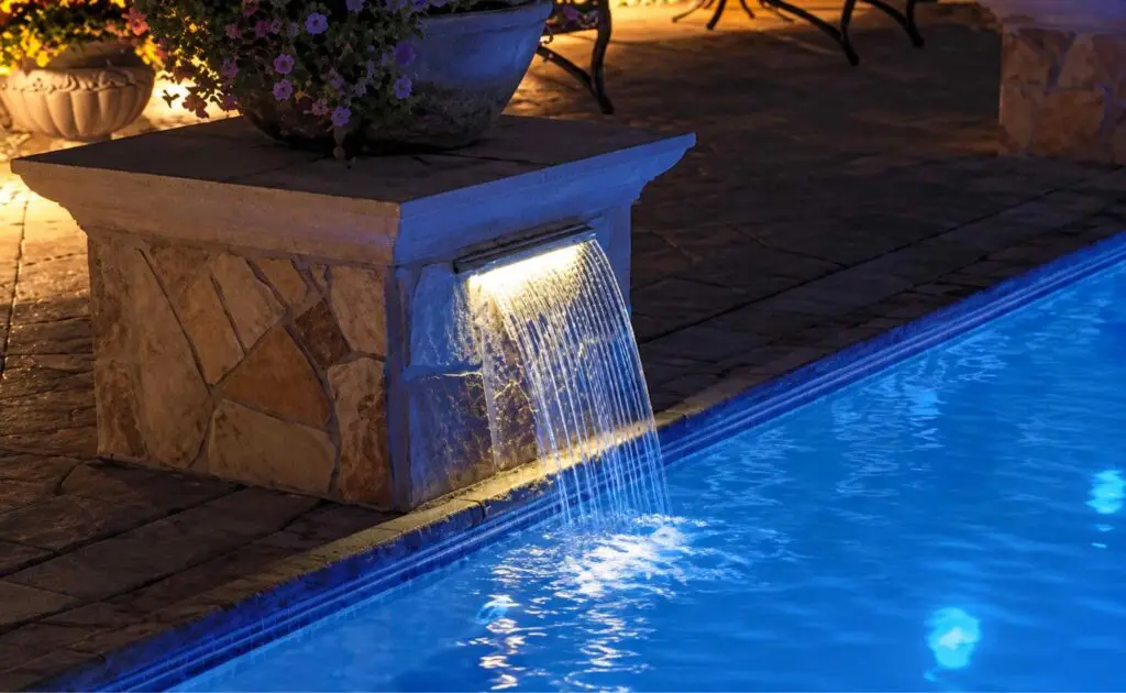 Pool cascade waterfall lit blue by color-changing LED lighting at night