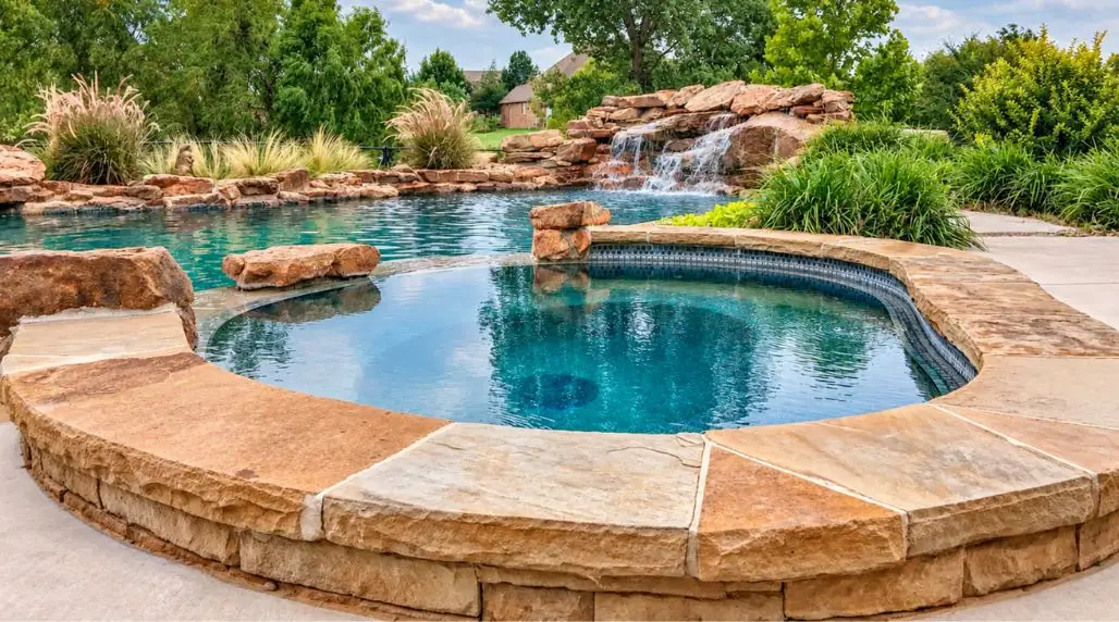 Luxury backyard swimming pool and spa with natural stone decking, rock waterfall, and landscaped garden