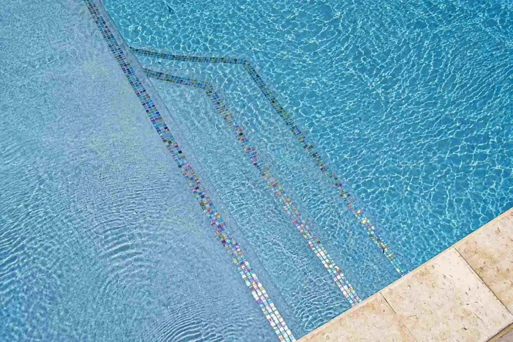 Overhead view of sunlit pool steps outlined in iridescent blue and gold glass mosaic tile