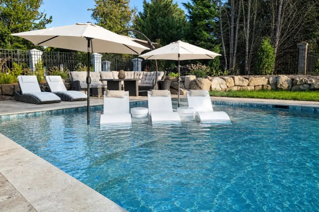 White in-water chaise loungers and side tables on a pool tanning ledge shaded by cantilever umbrellas