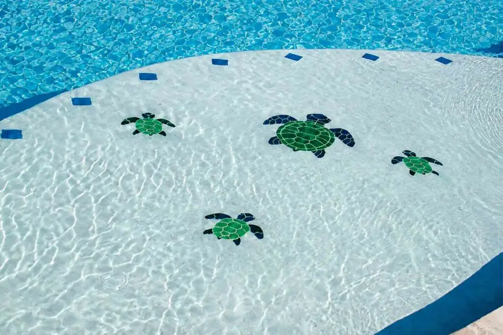 Green and blue sea turtle mosaic tiles set into the shallow tanning ledge of a swimming pool