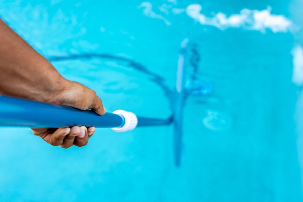 Hand holding a pool brush on a blue pole to clean the pool before closing it for winter