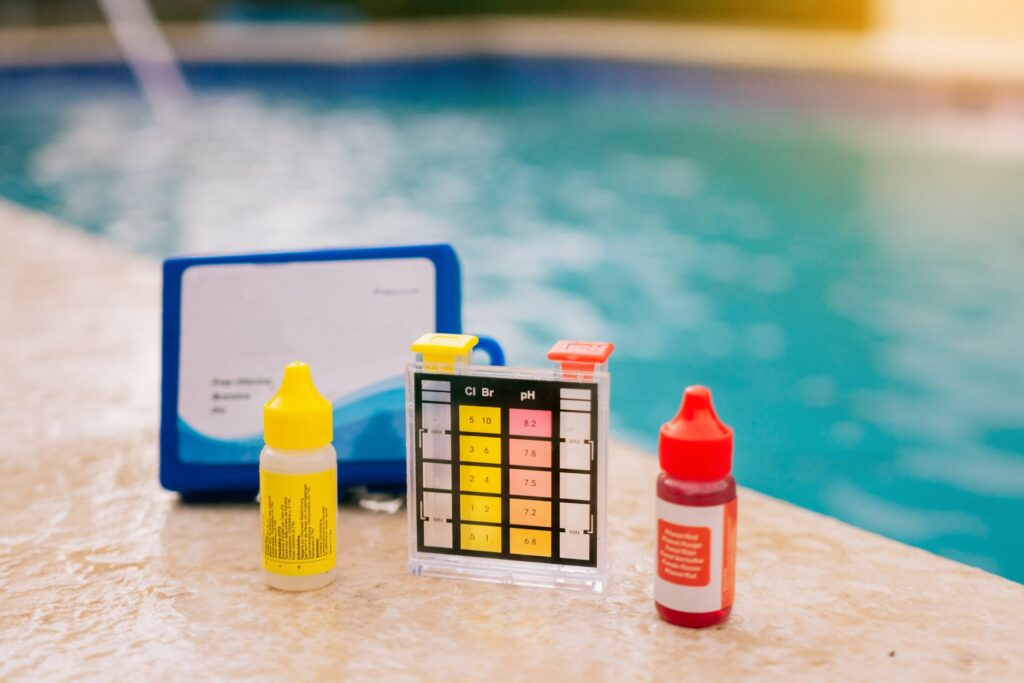 Pool test kit with pH and chlorine drops on the deck, used to balance water before you winterize an inground pool