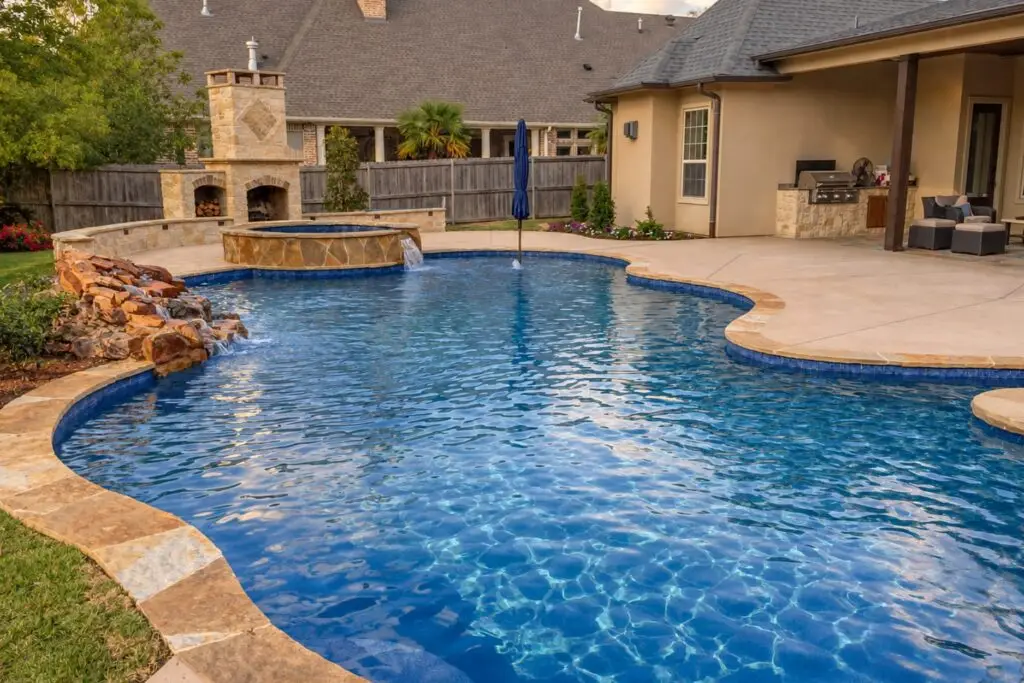 Freeform pool with flagstone coping, raised spa spillover, rock waterfall, and stone outdoor fireplace in a backyard