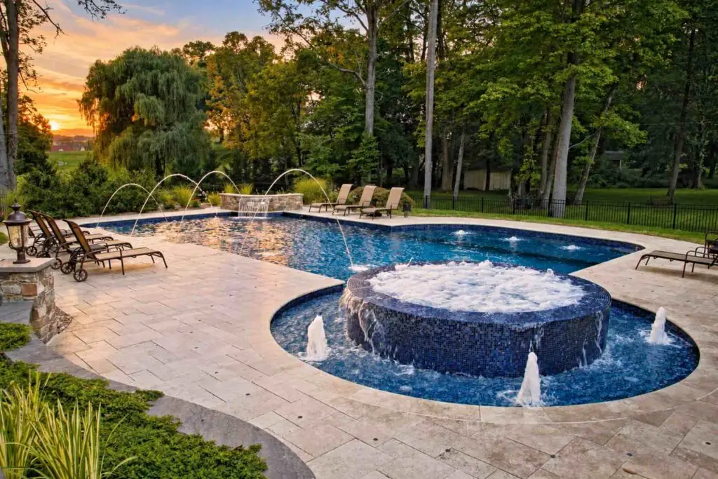 Raised round mosaic tile spa spilling into a pool with fountains and bubblers at sunset
