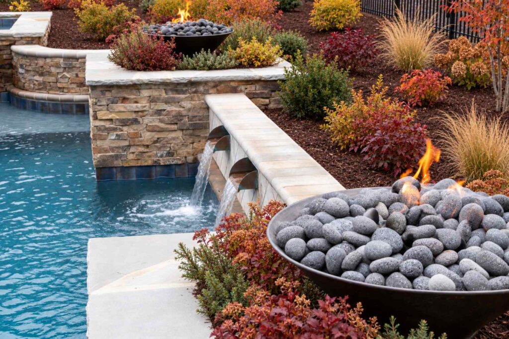 Pool with stacked stone wall, sheer descent water features, and fire bowls surrounded by colorful fall landscaping