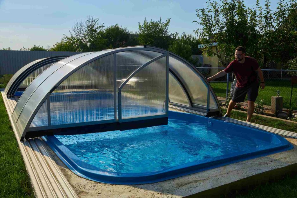Man sliding open a clear retractable enclosure over a backyard pool