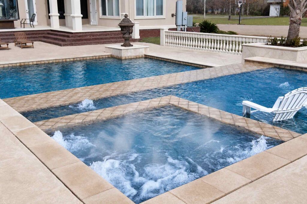 Heated spa with jets running and steam rising beside an inground pool on a cold day