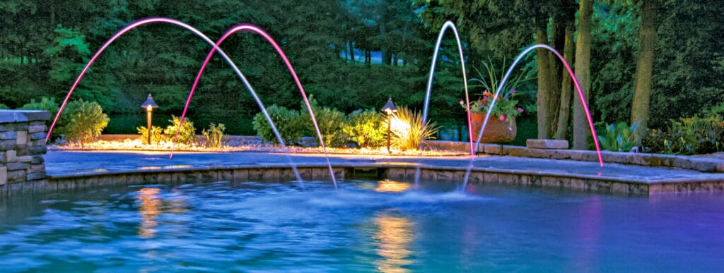 Pink and blue illuminated water laminars on backyard pool.