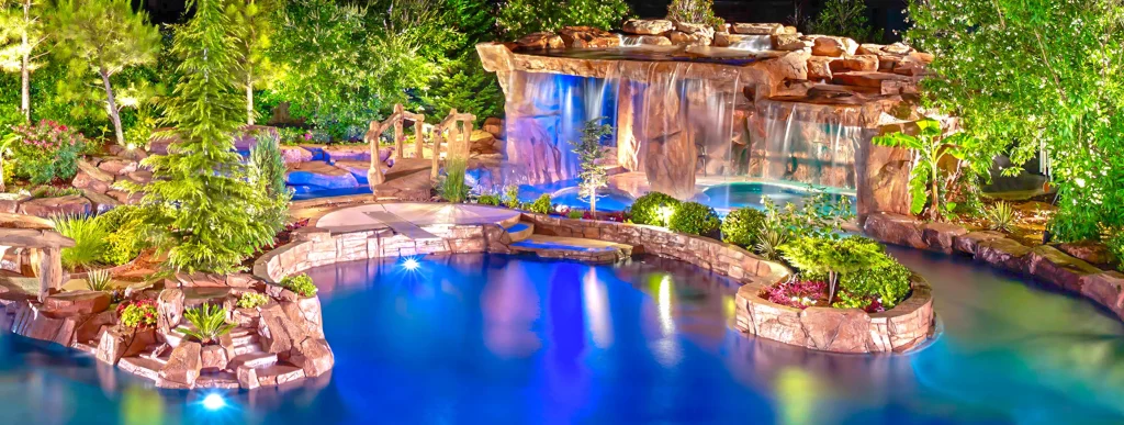 Lagoon-style pool with a large grotto waterfall surrounded by trees. at night.