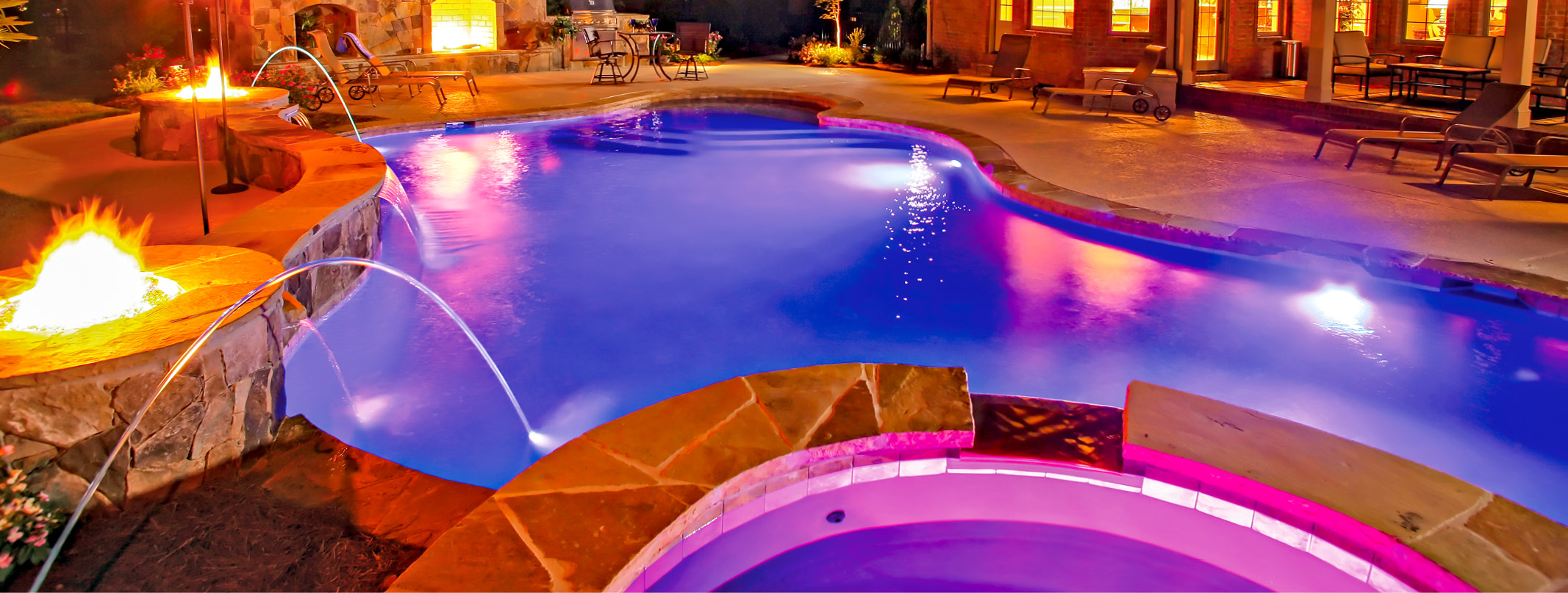 Custom pool & spa in Upstate South Carolina with pink and blue lighting at night.