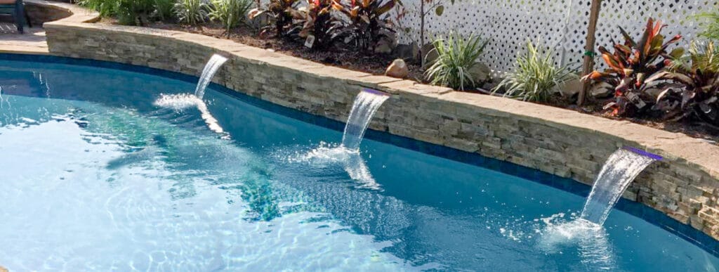 Trio of arced cascade waterfalls on stone-faced wall along an in-ground pool.