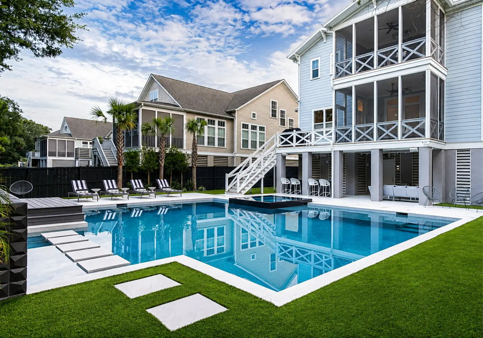 Custom inground swimming pool with a spacious white deck, modern coastal homes, and backyard seating area.