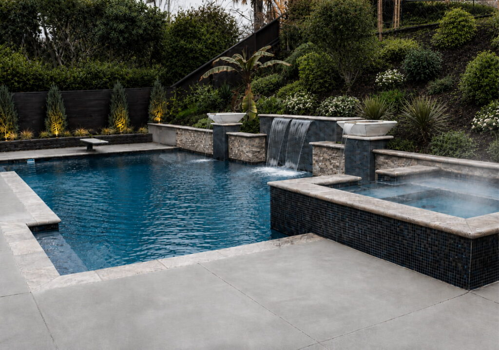 Rectangular gunite pool with attached raised spa, sheer descent waterfall wall, and two fire bowls in a landscaped backyard