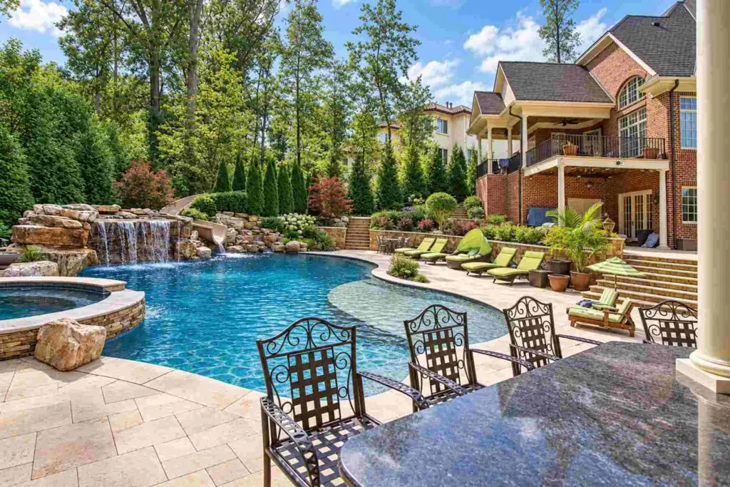 Swimming pool with a waterfall, slide, spa, and tanning ledge, seen from the bar seating at the kitchen