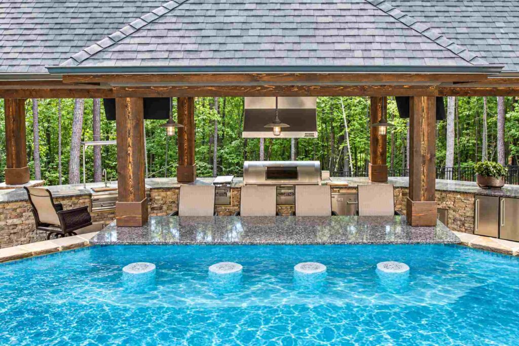 Poolside outdoor kitchen with in-pool barstools at a granite bar, viewed from inside the swimming pool
