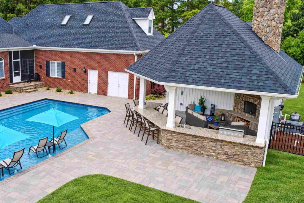 Poolside outdoor kitchen in a cabana between the house and the pool, with curved bar seating on a paver deck
