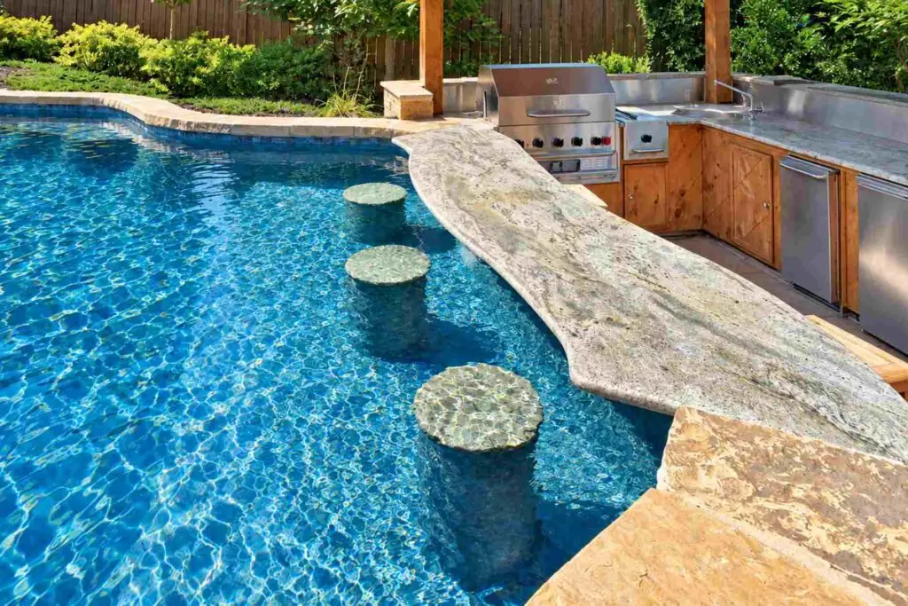 Swim-up bar with three in-pool barstools and a stone countertop connecting to a grill and outdoor kitchen