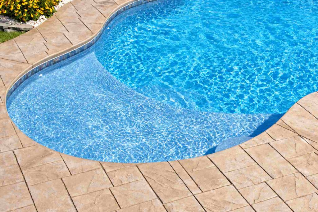 Stamped concrete cantilever deck extending over a freeform pool edge with no pool coping
