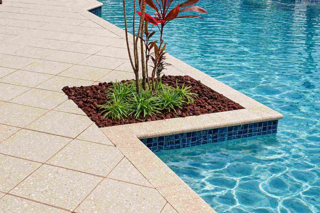 Pre-cast concrete pool coping with a rounded bullnose edge over blue tile next to a planter
