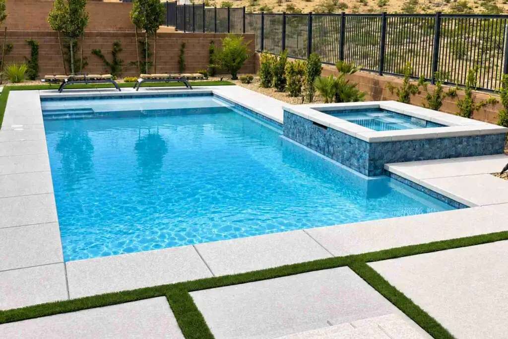 Light gray concrete paver coping around a modern rectangle pool and spa with turf strips