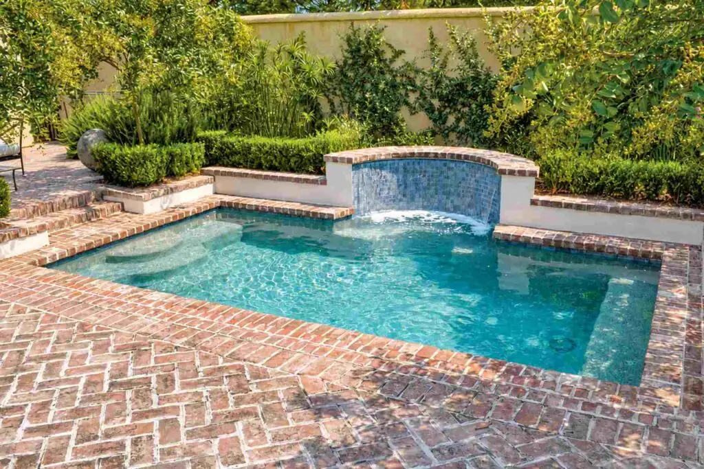 Brick pool coping and herringbone brick deck around a small pool with a water feature wall