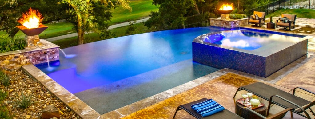 Fire bowls on a modern swimming pool are illuminated at sundown.