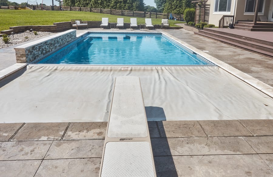Modern backyard pool with diving board, pool cover and elegant hardscape