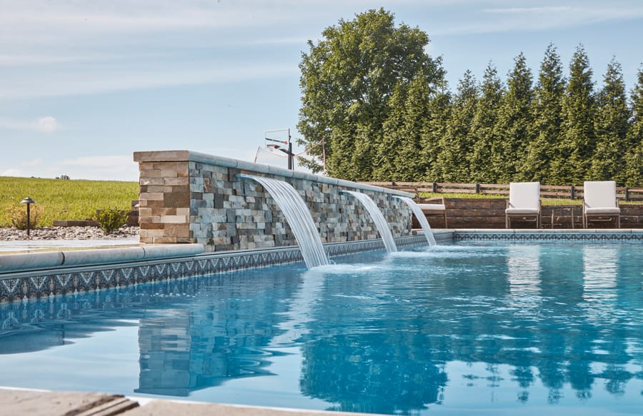 Geometric swimming pool with a wide sheer descent waterfall and modern stone wall