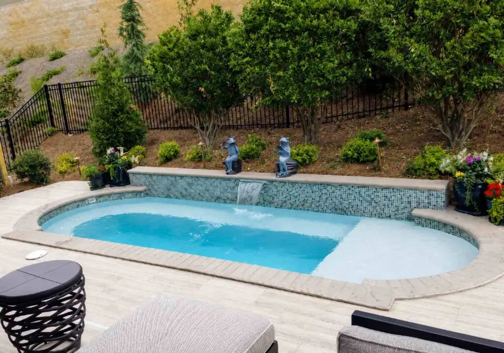 Oval cocktail pool with a glass tile wall, sun shelf, and patio lounge seating