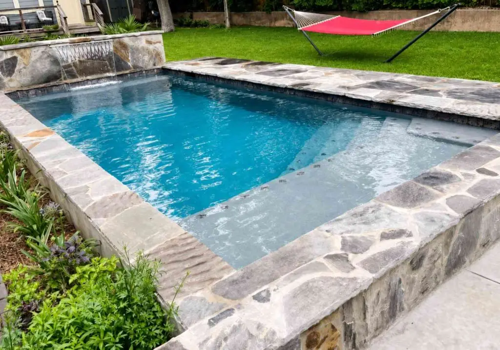 Shallow dipping pool with flagstone coping and a wide tanning ledge next to a lawn