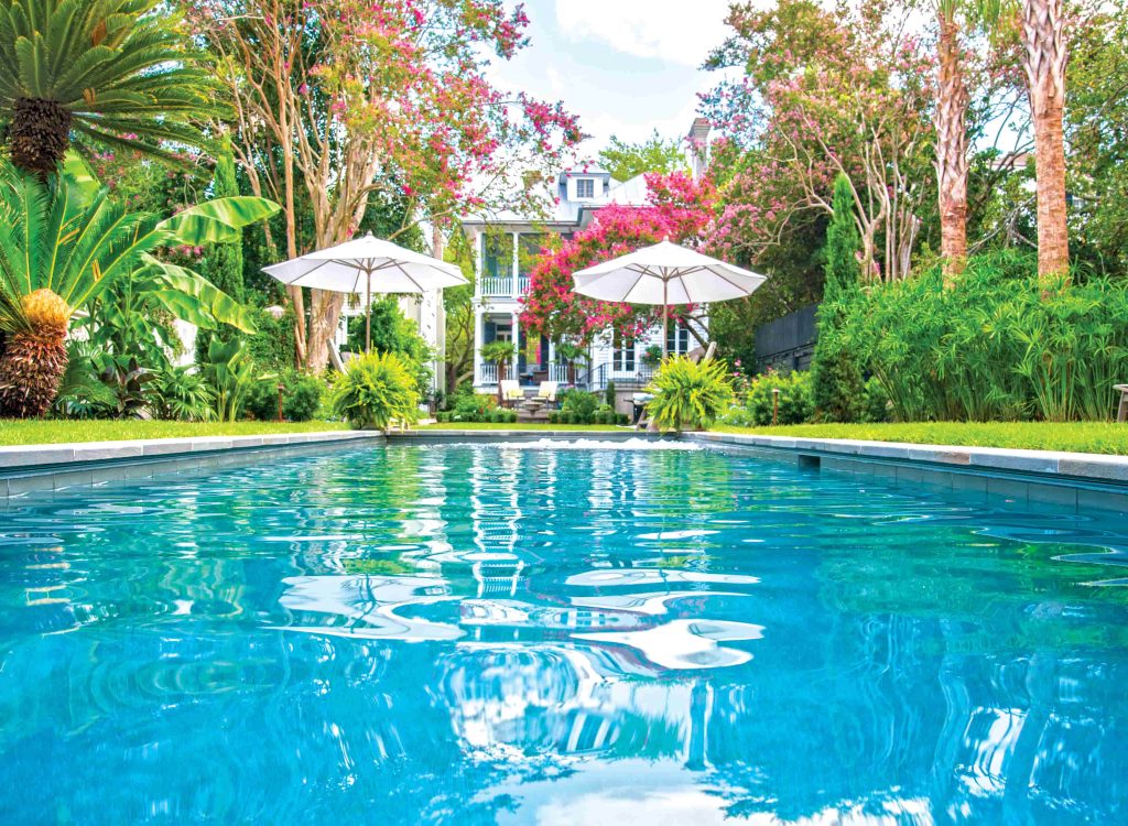 Backyard oasis with gunite swimming pool, vibrant garden, and shaded lounge area behind residential home