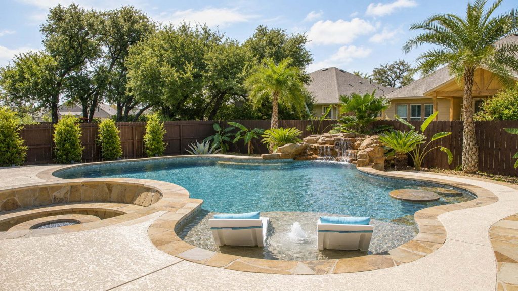 Blue Haven custom pool with tanning ledge, spa, rock waterfall, tropical landscaping, and wood privacy fence