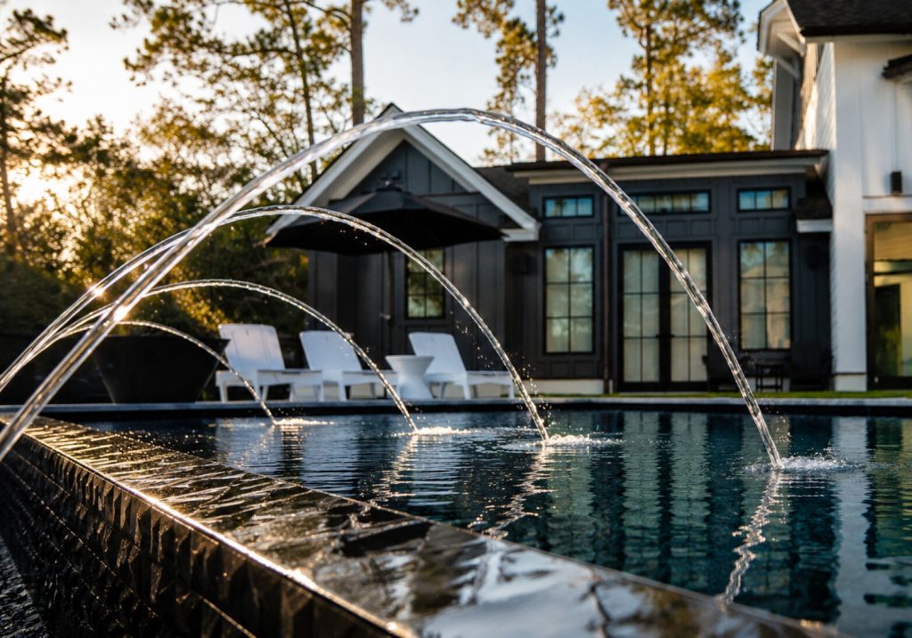 Multiple deck jets shooting arcing streams over a dark-tiled contemporary pool at golden hour