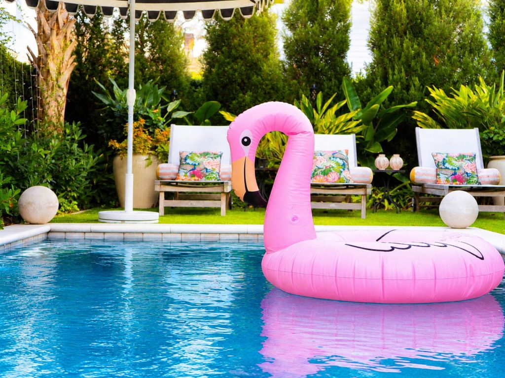Large pink inflatable flamingo pool float drifting in a landscaped Blue Haven backyard swimming pool.