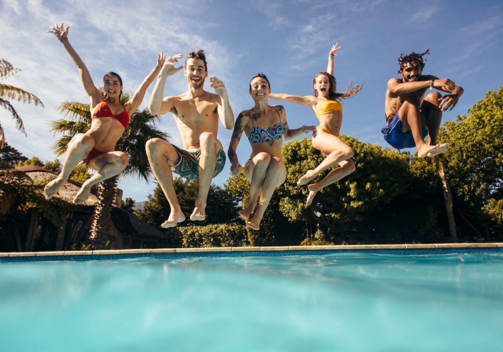 Group of friends jumping into a swimming pool on a sunny day