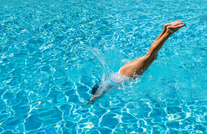 Person diving headfirst into a sparkling blue swimming pool with legs extended above the water