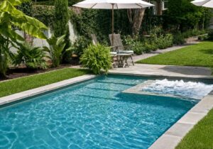 Backyard pool and raised spa surrounded by lush landscaping and a stone patio