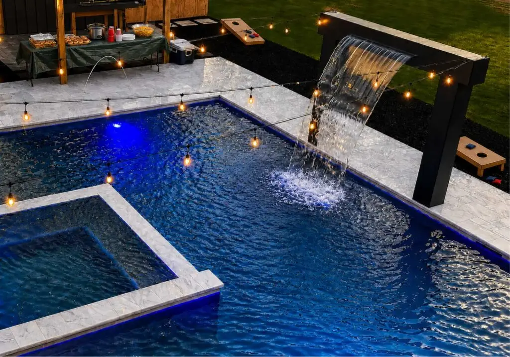 Backyard tailgating games at dusk with two cornhole boards beside a lit pool, string lights, and a food table