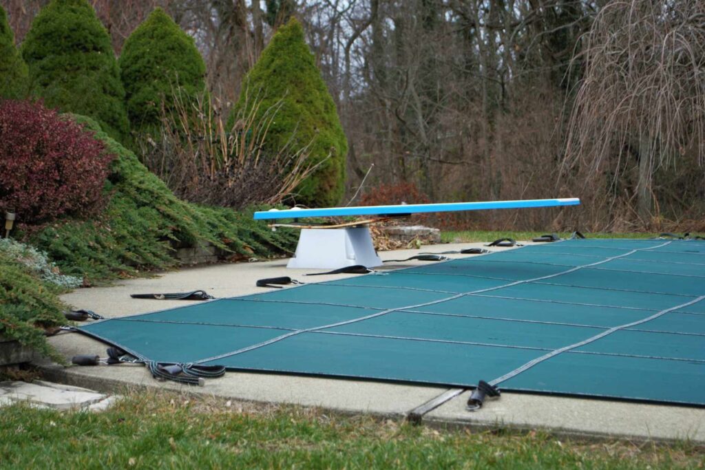 Green mesh winter safety cover strapped tightly over an in-ground pool after closing for the season